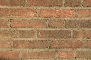a part of a brick wall of a dutch house with red brown bricks and cement