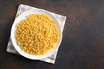 Raw ditalini pasta in white plate on brown. View from above. Copy space.