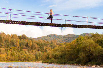 Obraz premium Young woman standing in tree yoga pose, meditating on bridge over mountain river.