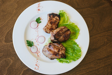Fried beef meat lies on a green lettuce leaf. Dish on a white plate on a brown table