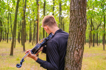 young male play on the violin in the summer park	