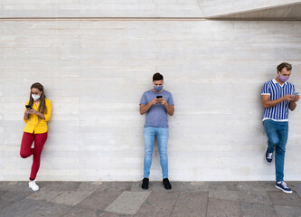 Obraz na płótnie Canvas Multiracial people standing in a line with social distance and looking at smartphones while wearing protective face mask - Coronavirus lifestyle