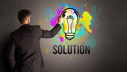 businessman drawing colorful light bulb with SOLUTION inscription on textured concrete wall, new business idea concept
