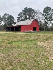 Red barn with a tin roof with trees behind it.