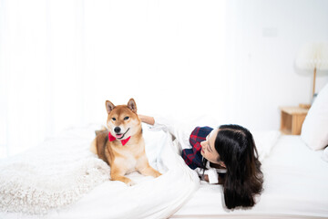 A young Asian woman lounging with a Shiba inu dog on a white bed.