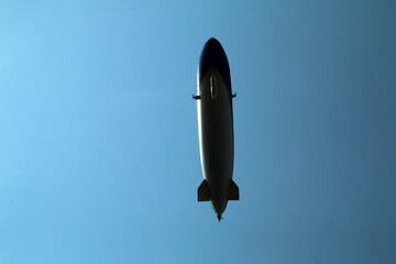 The detail of a lonely zeppelin flying high above in the blue sky. Almost only the silhouette is visible.  © shootingtheworld