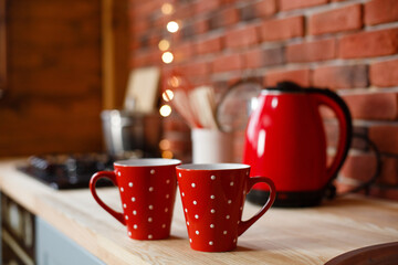 Kitchen in loft style with red accents. Red cups and electric kettle in loft kitchen on background...