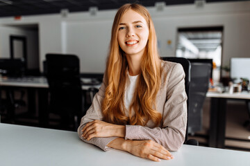 Smiling business young woman sitting at work desk in office - obrazy, fototapety, plakaty