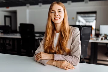 Tuinposter Smiling business young woman sitting at work desk in office © Shopping King Louie