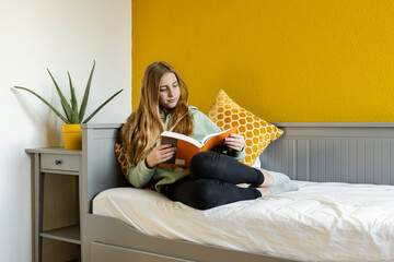 Young blond girl reading book at home