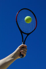 Raquete de tênis com bola amarela e fundo do céu azul