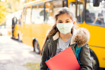 Secondary school girl learner in protective mask in front of school bus, ready to go home by bus....
