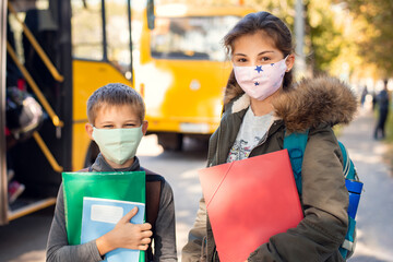 Boy and girl school learners going home after lessons. Children in protective medical masks near school bus.