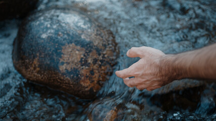 Person hand put in the flowing river or stream and is captivated by the water, close-up slow motion lifestyle nature concept