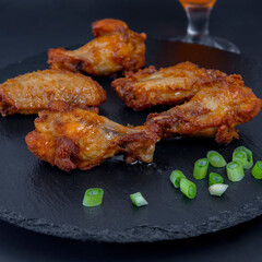 Fried chicken drumsticks on the black stone tray with some green onion