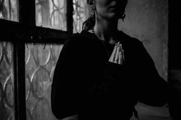 Dark and moody black and white photo of a woman doing yoga and meditation, breathing practices by the window of an old building