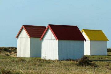 The tiny white beach cottages with colorful roofs at a beach by Gouville-sur-Mer in France in...