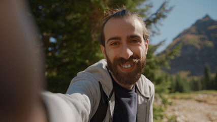 Hippie climber with his backpack behind him, with his handheld camera or phone, salutes the audience or the person he is talking, vlogger or video chat in nature concept