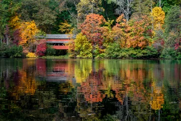 Fotobehang With a beautiful reflection on Lake Loretta in Alley Park, Lancaster, Ohio, the red George Hutchins Covered Bridge, surrounded by colorful autumn leaves, was constructed in 1865 at another location. © Kenneth Keifer