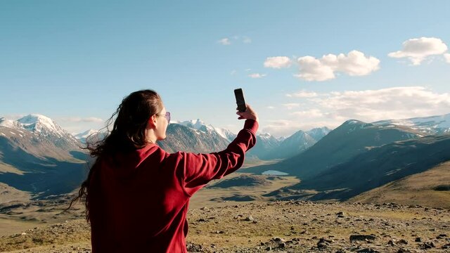 Brunette girl with long hair against mountains and wildlife background. A tourist photographs the landscape with his phone