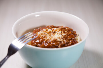 Spaghetti pasta with tomato sauce in white and blue bowl, white wooden background and resting straw plate and cutlery on the side, Brazilian cuisine copy space, top view. Food concept. Pasta concept.