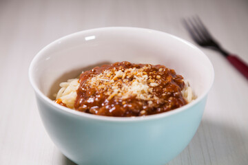 Spaghetti pasta with tomato sauce in white and blue bowl, white wooden background and resting straw plate and cutlery on the side, Brazilian cuisine copy space, top view. Food concept. Pasta concept.