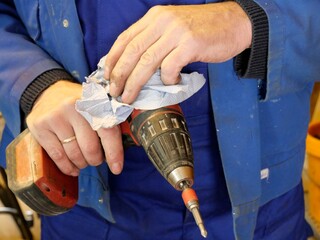 Handwerker im Blaumann reinigt Bohrmaschine mit Tuch