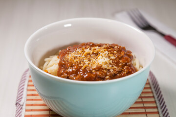 Spaghetti pasta with tomato sauce in white and blue bowl, white wooden background and resting straw plate and cutlery on the side, Brazilian cuisine copy space, top view. Food concept. Pasta concept.