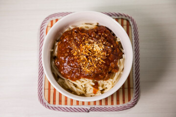 Spaghetti pasta with tomato sauce in white and blue bowl, white wooden background and resting straw plate and cutlery on the side, Brazilian cuisine copy space, top view. Food concept. Pasta concept.