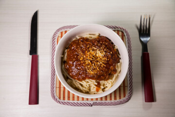 Spaghetti pasta with tomato sauce in white and blue bowl, white wooden background and resting straw plate and cutlery on the side, Brazilian cuisine copy space, top view. Food concept. Pasta concept.
