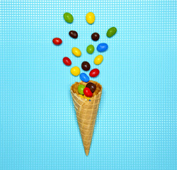 Ice cream cone flat lay image with colorful sweets, candy packing into the cone. Creative layout isolated on blue retro background. Food concept. top view, copy space for text
