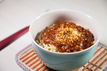 Spaghetti pasta with tomato sauce in white and blue bowl, white wooden background and resting straw plate and cutlery on the side, Brazilian cuisine copy space, top view. Food concept. Pasta concept.