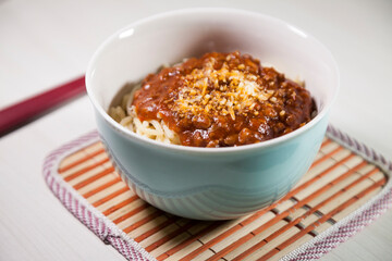 Spaghetti pasta with tomato sauce in white and blue bowl, white wooden background and resting straw plate and cutlery on the side, Brazilian cuisine copy space, top view. Food concept. Pasta concept.