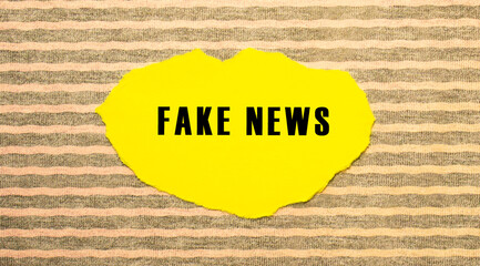 Yellow torn paper with the text FAKE NEWS on a gray-pink background.