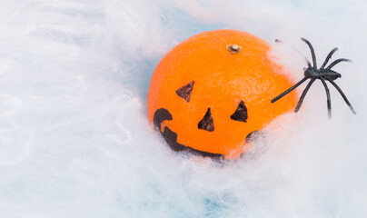 Bright orange Halloween scary tangerine emotion face on white spider web background with spiders, selective focus