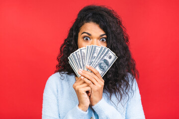 Portrait of a cheerful young curly african american woman holding money banknotes and celebrating isolated over red background.