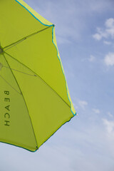 part of a green umbrella seen from below on which the beach is turned upside down, in the background you can see the blue sky with some white clouds
