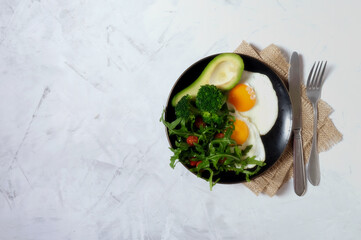 Keto breakfast concept. Fried eggs with avocado, broccoli and arugula. Place for text.