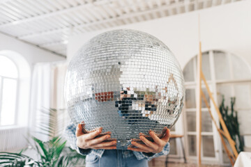 Young woman holding big disco ball in hands.