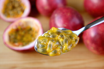 Closeup of the flesh and seeds of ripe passion fruit on a spoon with blurry whole fruits in background