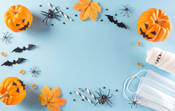 Halloween decorations made from pumpkin, paper bats and surgical face mask on pastel blue background. Flat lay, top view of Halloween celebration during covid-19 pandemic situation.