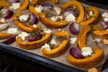 Baked pumpkin or squash slices with red onions, garlic, feta cheese and thyme on a tray, autumn...