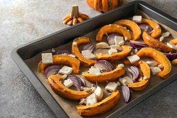 Raw pumpkin or squash slices on a baking tray with red onions, garlic and feta cheese, cooking with...