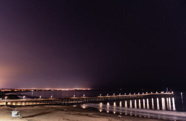 Pier lamps reflect in the ocean water under the Ventura Pier with constellation stars in sky above.