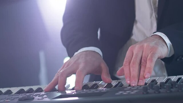 Man in a suit plays six-string electric synthesizer at concert. Close-up footage of musiian's hands at party with strobe disco lights.