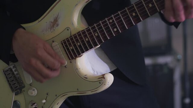 Man in a suit plays six-string electric guitar at concert. Close-up footage of musiian's hands at party with strobe disco lights.