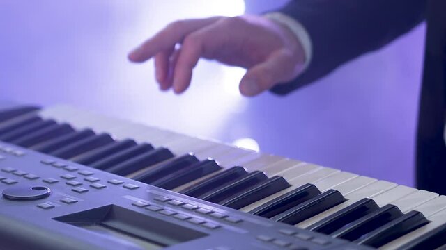 Man in a suit plays six-string electric synthesizer at concert. Close-up footage of musiian's hands at party with strobe disco lights.