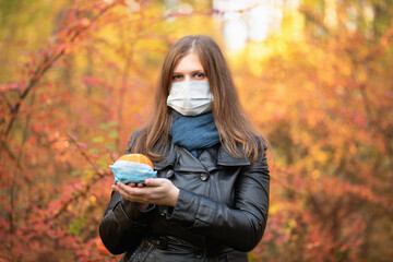 A girl in a medical mask with a pumpkin in leather jackets on the background of an autumn forest....