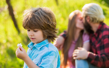 Pledge of love. Little child with couple kissing on background. Small child hold spring flower. Cute boy child sunny day. Child care. Family life. Blossoming nature. New life and growth. Childhood