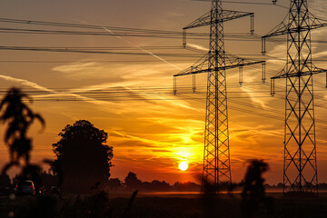 Die Sonne geht hinter einer Stromtrasse an der Kölner Stadtgrenze auf.